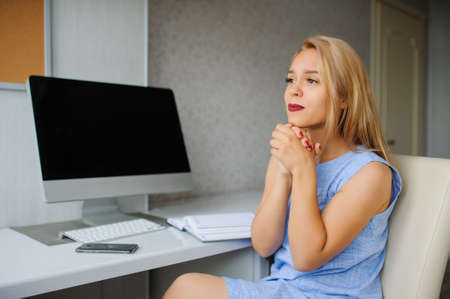 Serious young woman in blue dress working on a pc in her officeの写真素材