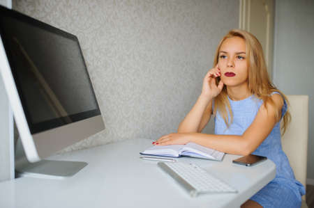 Serious young woman in blue dress working on a pc in her officeの写真素材