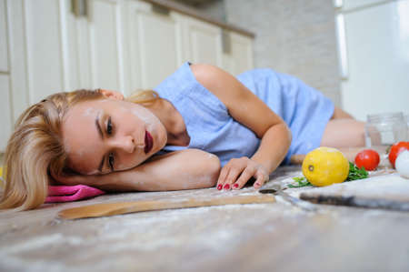 Concept of desperate housewife lying on the floor in her kitchen with flour on her faceの写真素材