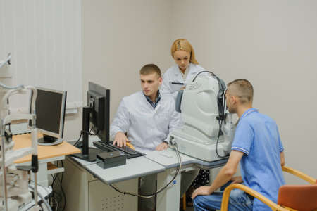 Young beautiful doctor/eye specialist/optometrist in an ophthalmologic clinic examines a patient with Tomography in Optical Coherence (OCT) procedure and explain to the student the resultの写真素材