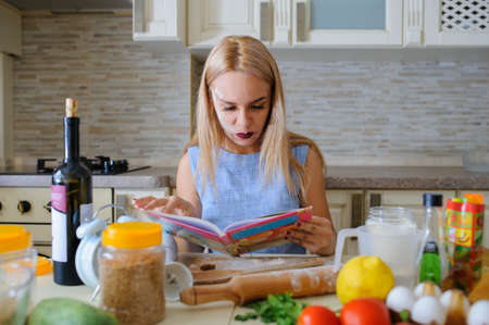 Concept of happy housewife reading cooking book in her kitchen and smileの写真素材