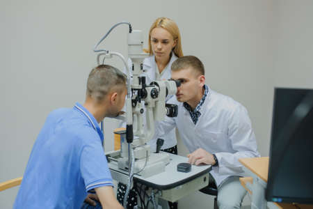 Young beautiful two doctors /eye specialist/optometrist in an ophthalmologic clinic examines a woman patient with biomicroscopy with slit lamp procedure.の写真素材