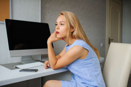 Serious young woman in blue dress working on a pc in her officeの写真素材