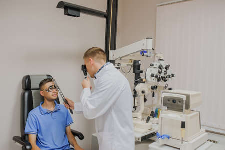 Young beautiful doctor/eye specialist/optometrist in an ophthalmologic clinic dooing to a patient eye test with ophthalmoscopeの写真素材