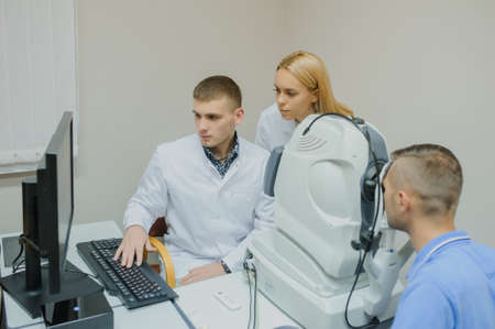 Young beautiful doctor/eye specialist/optometrist in an ophthalmologic clinic examines a patient with Tomography in Optical Coherence (OCT) procedure and explain to the student the resultの写真素材