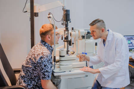 Young beautiful doctor/eye specialist/optometrist in an ophthalmologic clinic examines a patient with biomicroscopy with slit lamp procedure.の写真素材