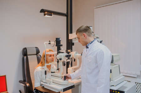 Young beautiful doctor/eye specialist/optometrist in an ophthalmologic clinic examines a woman patient with biomicroscopy with slit lamp procedure.の写真素材