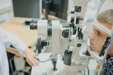Young beautiful two doctors /eye specialist/optometrist in an ophthalmologic clinic examines a woman patient with biomicroscopy with slit lamp procedure.の写真素材