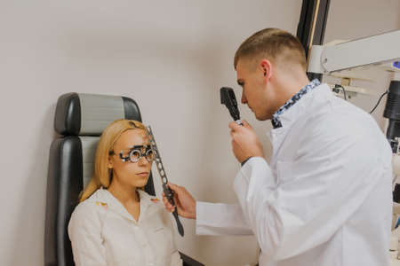 Young beautiful doctor/eye specialist/optometrist in an ophthalmologic clinic dooing to a patient woman ophthalmoscopyの写真素材