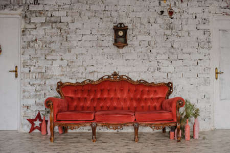 Vintage royal red sofa in a room, white brick wall with wood clock and painted bottleの写真素材