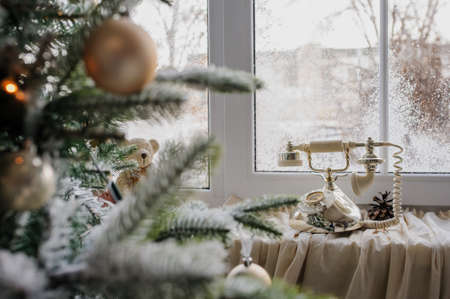 Close up a vintage phone on the window and christmas tree with presents, balls, and artificial snowの写真素材
