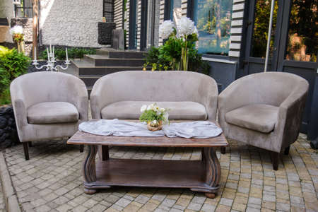 Outdoor composition from vintage sofa and armchair with table in front of it with vase with white eustoma on itの写真素材