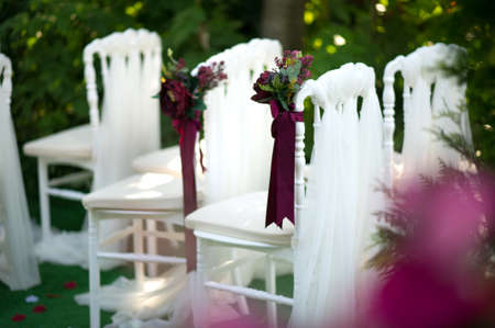 White vintage style chairs decorated with red / claret flowers: ranunculus and peony. Part of a wedding receptionの写真素材