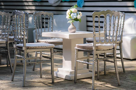 Party wedding decoration outdoor. Vintage metallic silver style chairs and table with flowers decoration on it from: roses, hortensia and ranunculusの写真素材