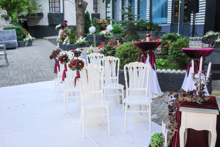 White vintage style chairs decorated with red / claret flowers: ranunculus and peony. Part of a wedding receptionの写真素材