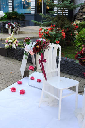 White vintage style chairs decorated with red / claret flowers: ranunculus and peony. Part of a wedding receptionの写真素材