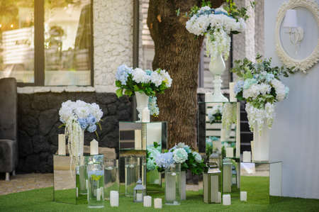 Party wedding decoration outdoor. Vintage metallic style, flowers decoration  from: roses, hortensia and ranunculus. Vase from mirror. Candle on the floorの写真素材