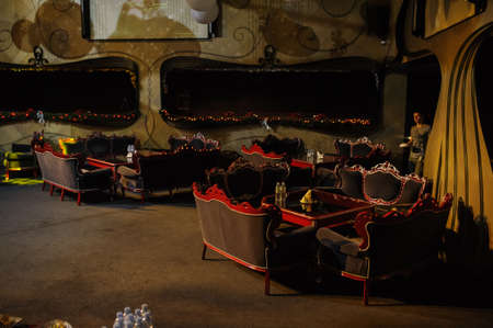 A banqet hall dark with round tables with red and gold elementsの写真素材