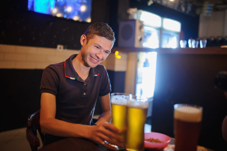 Young handsome man in the bar with two beers on the table, wearing a t-shirt and smiling.