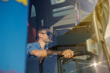 Young handsome man at the wheel is looking away from the bus, wering a t-shirt with sunglasses and...