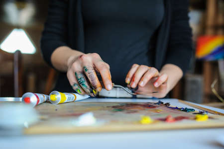 Close up dirty Hands of female artist on the palette with different paints and paintbrush in art studio.の写真素材