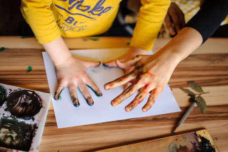 Young mother and her son playing with color paints in art studio. Dirty hands with color on them and impression on the white paper.の写真素材