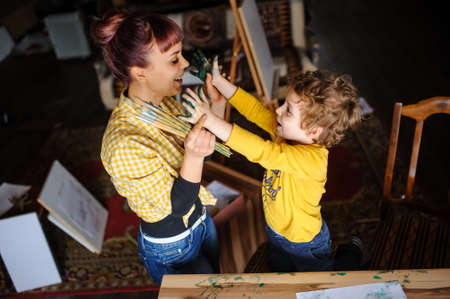 Young mother and her son playing with color paints in art studio and having dirty hands with color on them and dirty faceの写真素材