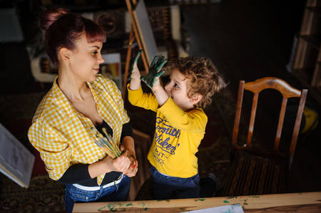 Young mother and her son playing with color paints in art studio and having dirty hands with color on them and dirty faceの写真素材