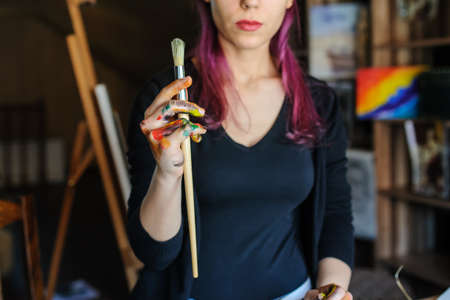 Selective focus on female artist dirty hands with different paints on them that Holding paint brushes in art studio.の写真素材