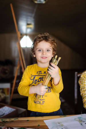 Young boy playing with color paints in art studio and having dirty hands with color on them that holding paint brushes and smileの写真素材