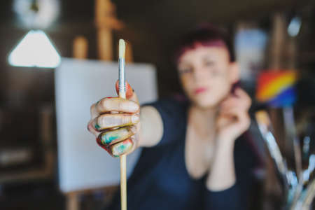 Selective focus on female artist dirty hands with different paints on them that Holding paint brushes in art studio.の写真素材