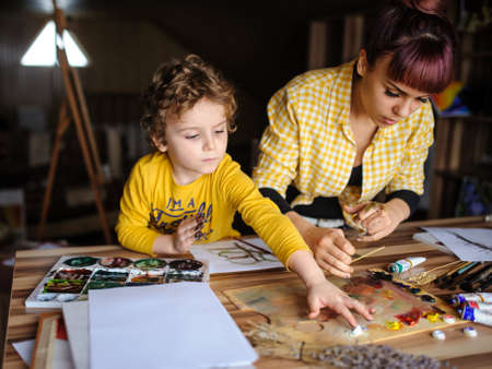 Young mother and her son playing with color paints in art studio and having dirty hands with color on themの写真素材