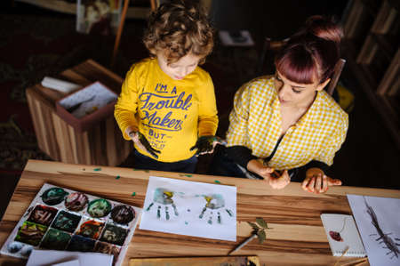 Young mother and her son playing with color paints in art studio. Dirty hands with color on them and impression on the white paper.の写真素材