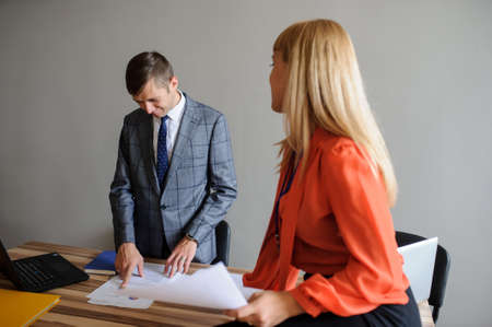 A business woman and man at a wooden office desk  working at the project on the paper and computer, grey backgroundの写真素材