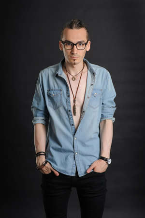 Young handsome boy in denim shirt and glases, curly hair, hands in pockets,
with black backgroundの写真素材