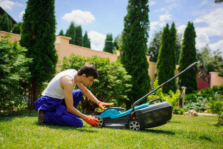 Young handsome  gardener man is cutting the grass with the mowerの写真素材
