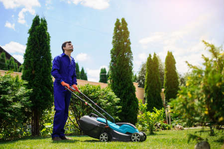 Young handsome  gardener man is cutting the grass with the mowerの写真素材