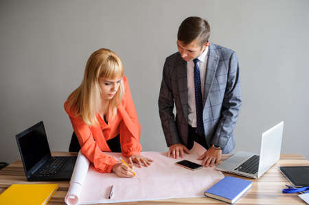 A business woman and man at a wooden office desk  looking at the project on the paper, working with pen and compassの写真素材