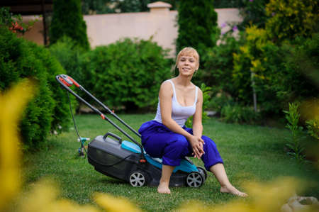 Young handsome  gardener girl is cutting the grass with the mowerの写真素材