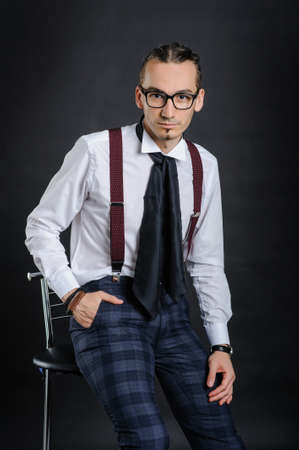 Young handsome boy in white shirt with tie sitting on the chair, with black backgroundの写真素材