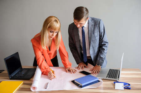 A business woman and man at a wooden office desk  looking at the project on the paper, working with pen and compassの写真素材
