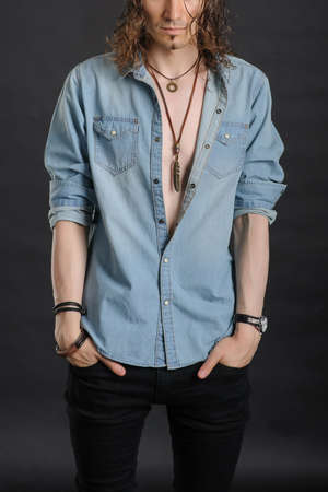 Young handsome boy in denim shirt and glases, curly hair, hands in pockets,
with black backgroundの写真素材