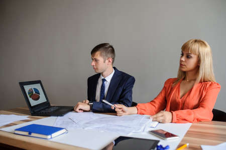 A business woman and man at a wooden office desk  looking at the project on the paper and computer with charts, grey backgroundの写真素材