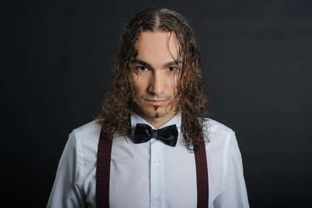 Young handsome boy in white shirt with bowtie and curly hair, with black backgroundの写真素材