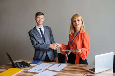 A business woman and man at a wooden office desk  handshaking, grey backgroundの写真素材