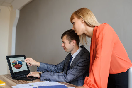 A business woman and man at a wooden office desk  working at the project on the paper and computer,...