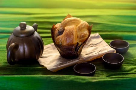 Three cups, a kettle of ceramics and a cake on the green background, close viewの写真素材