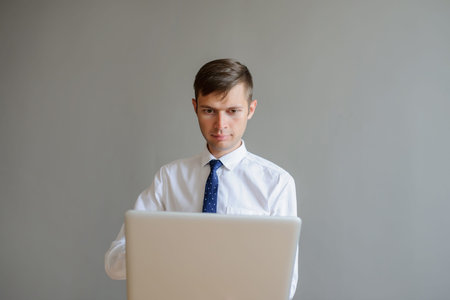 A business man in white shirt to the tie looking at his computer, gray background