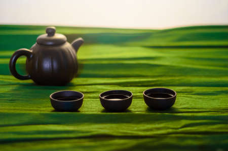 Three cups and a kettle of ceramics on the green background, close viewの写真素材