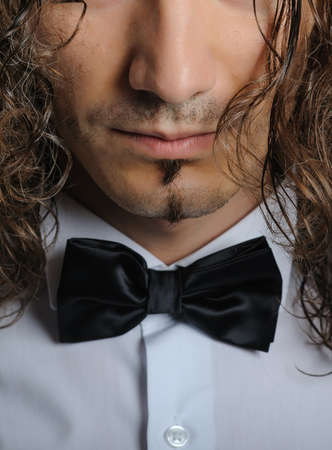 Young handsome boy in white shirt with bowtie and curly hair, with black backgroundの写真素材